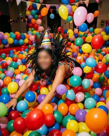 Diving into a huge ball pit of party balloons in a party hat