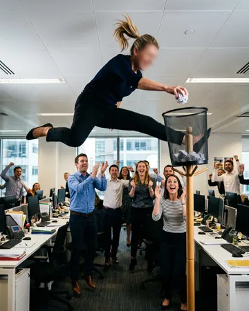 Slam-dunking a paper ball into an office bin as colleagues cheer